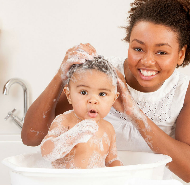 Mom bathing baby's hair in bathtub smiling for camera with white shirt